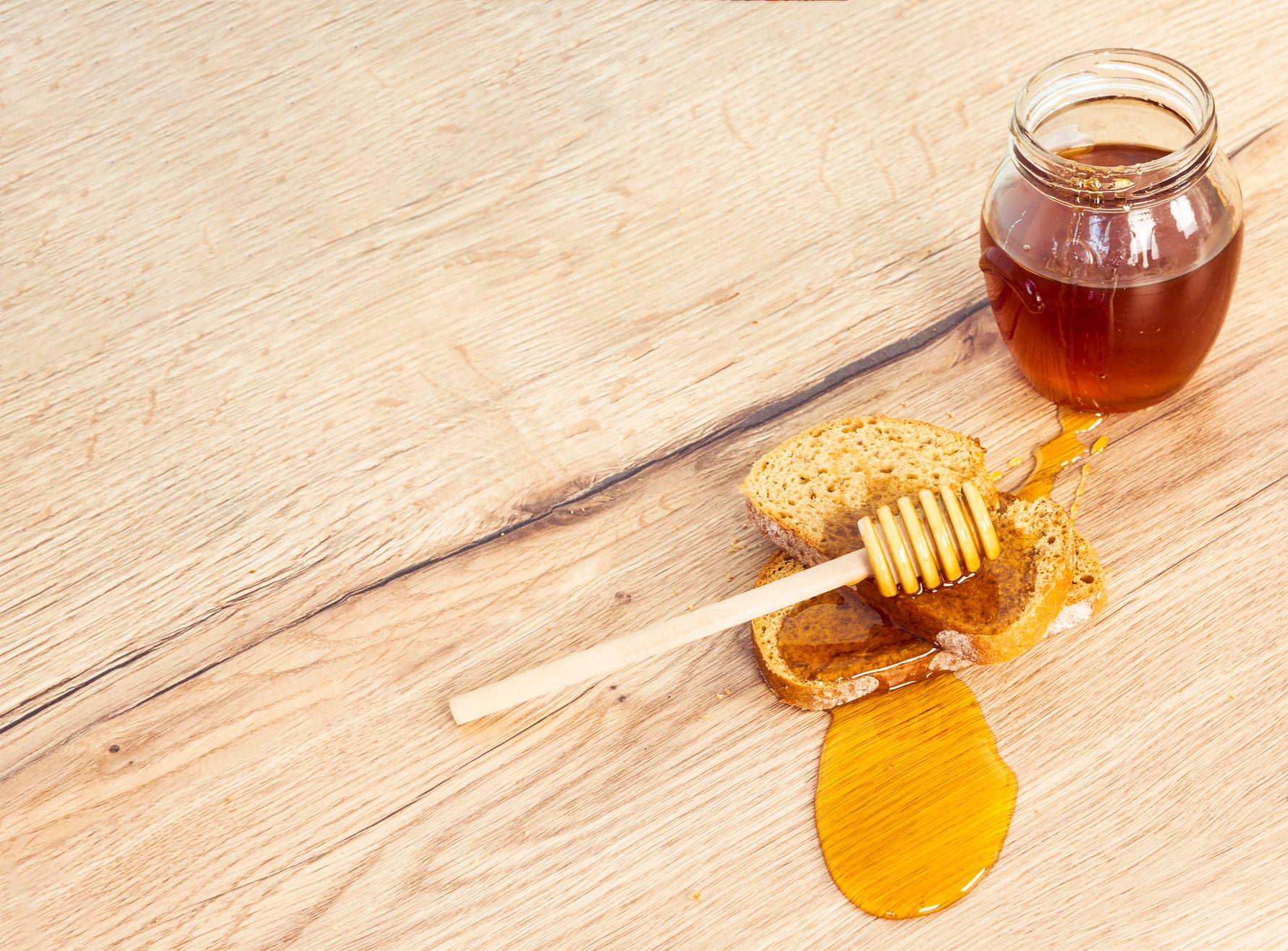 Golden Greek thyme honey being lifted with a wooden honey dipper on a rustic table