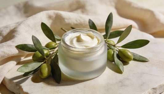 Natural antioxidant face cream with fresh olive leaves on a pale stone surface